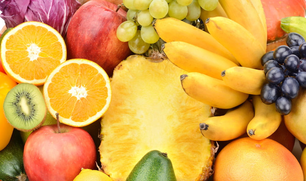 Bunte Auswahl an Obst, darunter Äpfel, Trauben, Bananen, Ananas und Orangen, auf einem Spritzschutz.