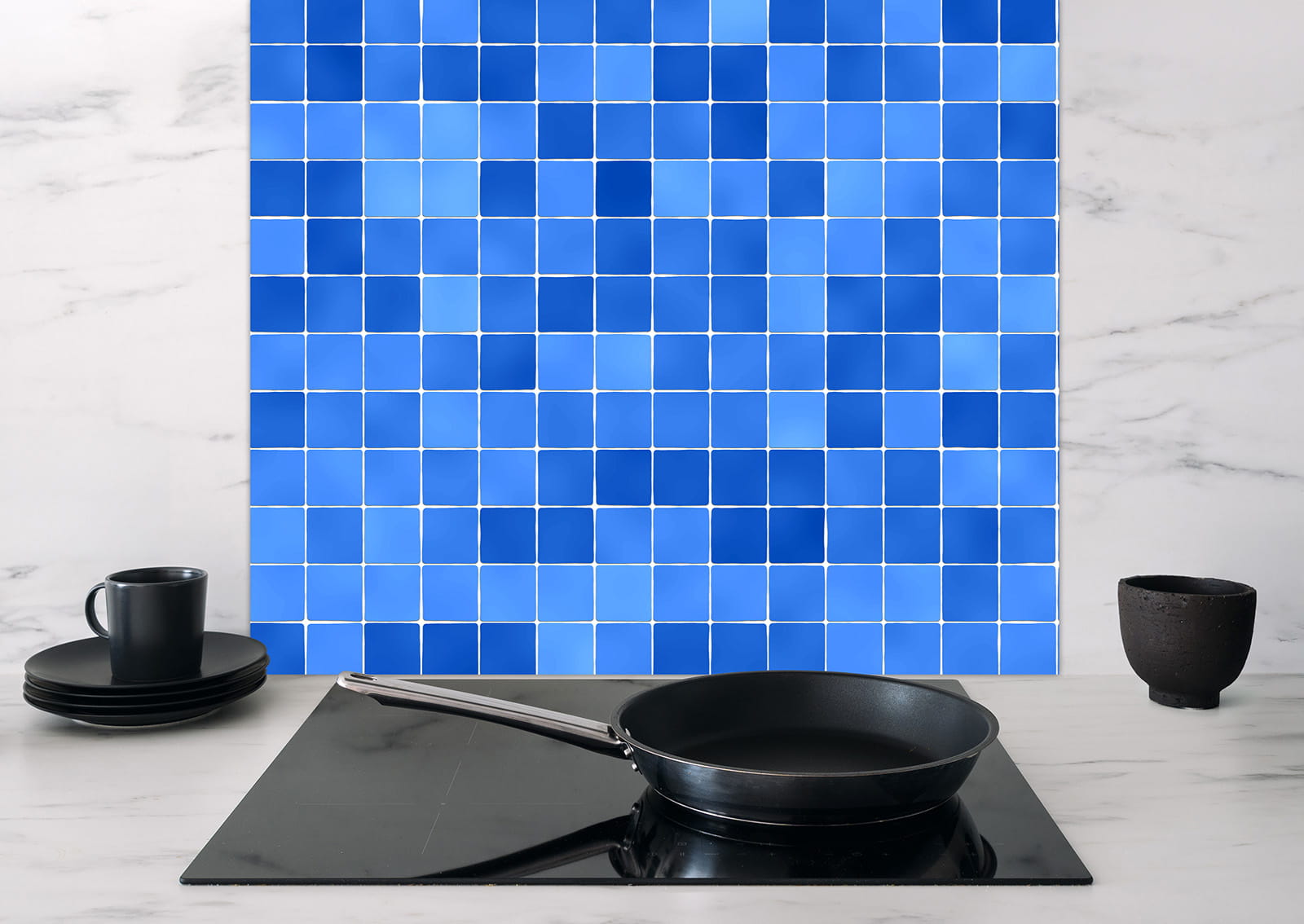 Spritzschutz "Blaue Quadrate" von ENTDECKER, mit blauen Mosaikfliesen hinter einem Herd, Pfanne und Geschirr sichtbar.
