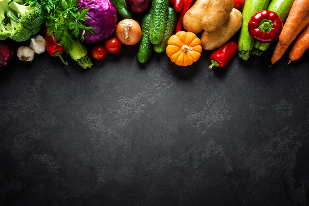 Buntes Gemüse, darunter Brokkoli, Karotten, Paprika, Zucchini, und Kürbis, auf dunklem Hintergrund.
