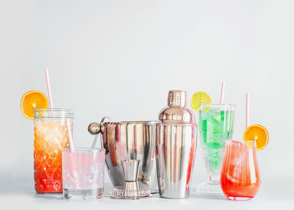 Cocktail-Set mit Shaker und Spritzschutz, bestehend aus verschiedenen bunten Cocktails in Gläsern, einem Eiseimer und einem Messbecher.