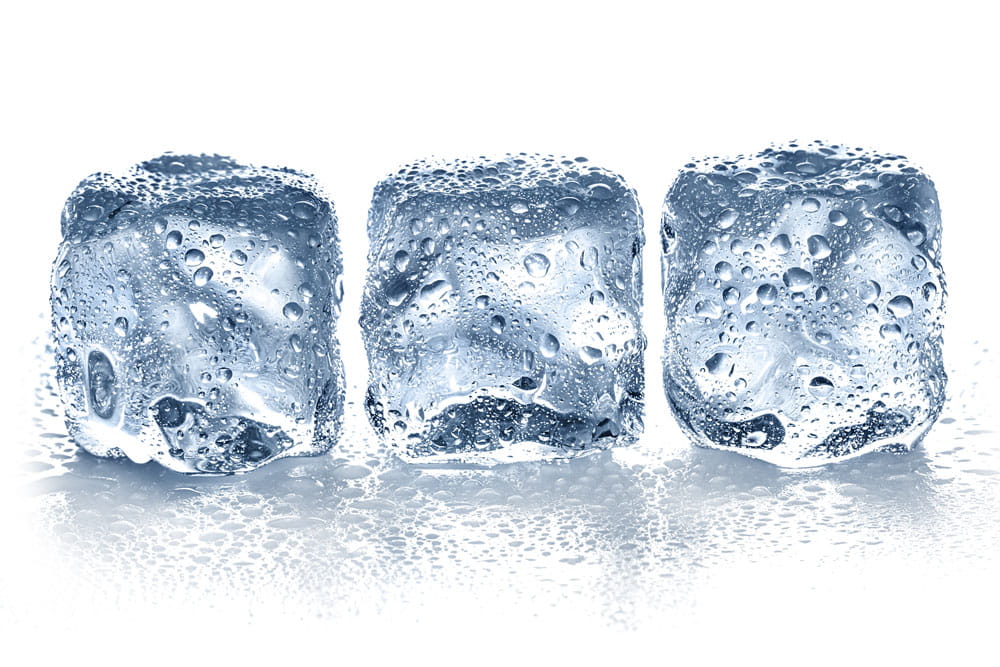 Drei klare Eiswürfel mit Wassertropfen auf der Oberfläche, auf einem hellen Untergrund.