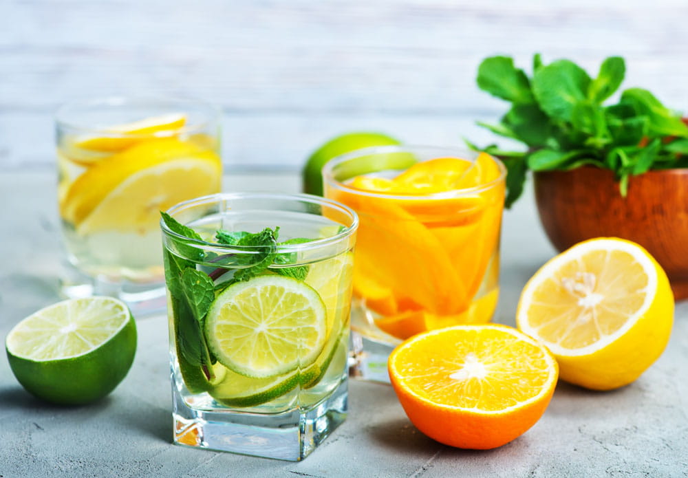 Cocktails mit frischen Zitrusfrüchten und Minze in Gläsern, darunter Limetten- und Zitronenscheiben, sowie eine Schüssel mit Orangenscheiben.