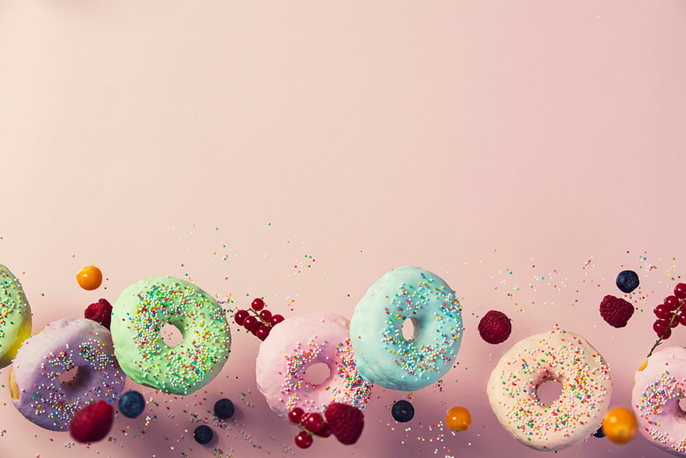 Bunte Donuts mit Zuckerguss und Streuseln, umgeben von frischen Beeren und Früchten.