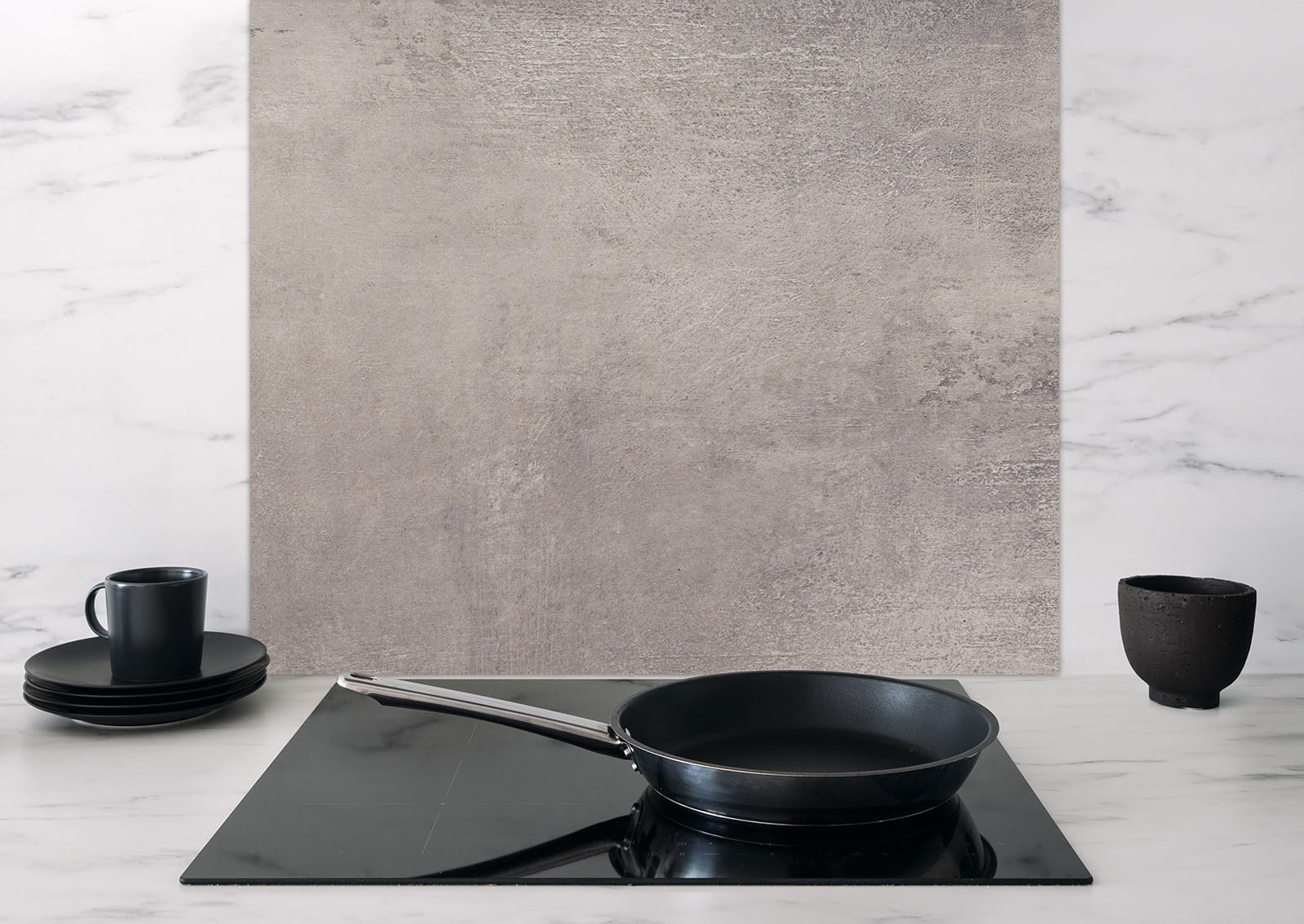 Spritzschutz 'Natuerlicher Beton' von ENTDECKER, graue Betonoptik, in einer modernen Küche mit Pfanne und Geschirr.