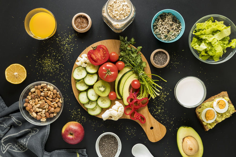 Gemüseplatte mit Gurken, Tomaten, Paprika, Karotten und Salat auf einem Holzbrett, umgeben von verschiedenen Zutaten und Getränken.