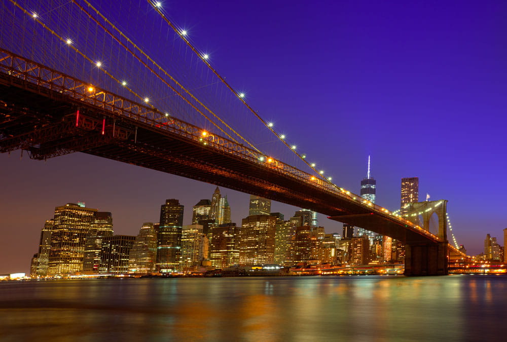 Die Brooklyn Bridge bei Nacht mit beleuchteter Skyline von New York im Hintergrund.