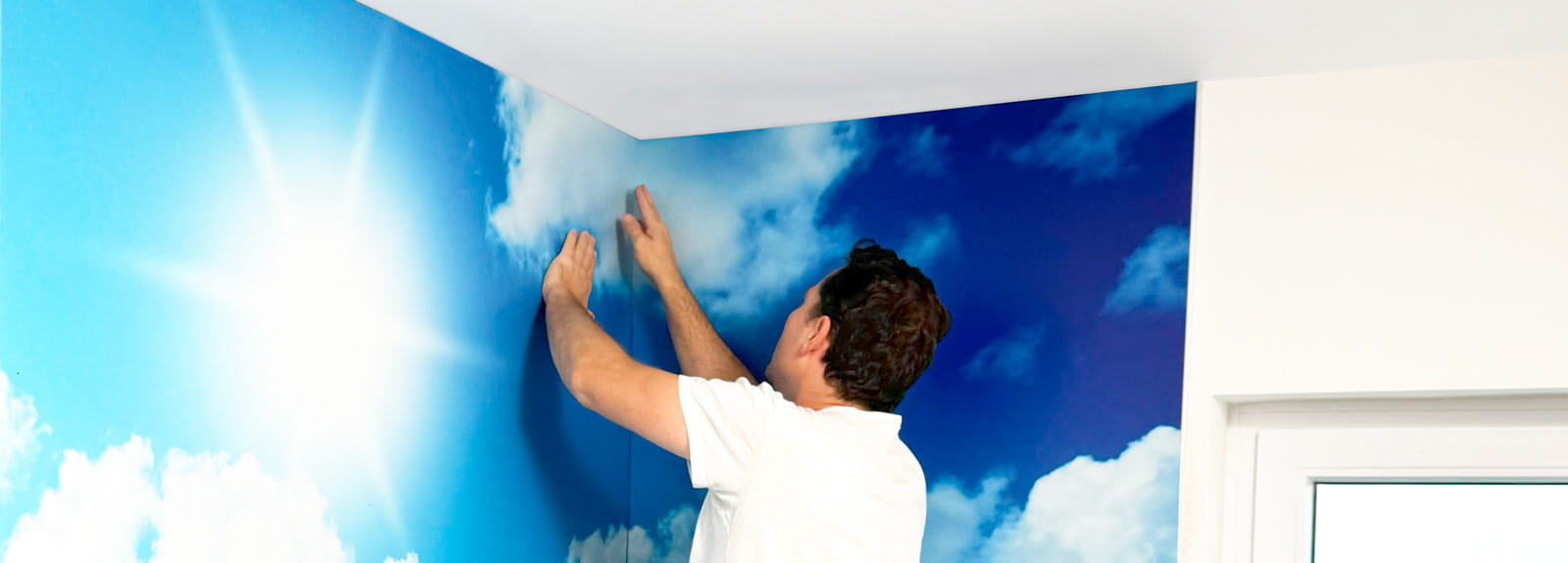 Wanddekoration anbringen Mann bringt eine Wanddekoration mit Himmel- und Wolkenmotiv an.